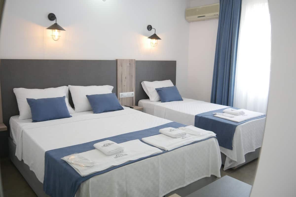 A hotel room with two beds, each with a blue bedspread and white linens, and two wall-mounted lights.