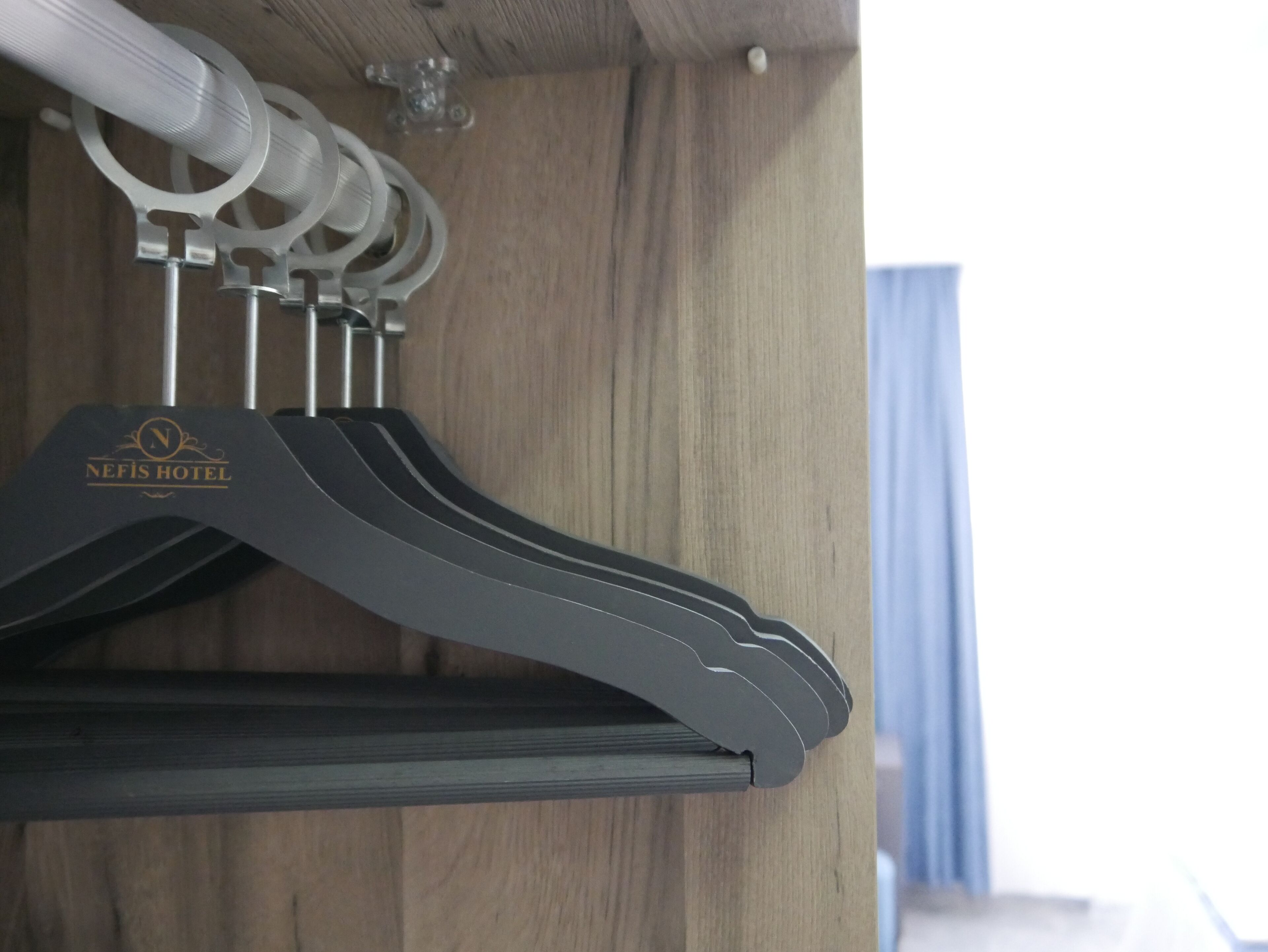 A set of black hangers with a logo on the left, hanging on a wooden wall.