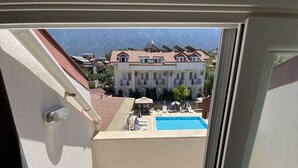 A balcony with a view of a swimming pool, a building with balconies, and a mountainous landscape in the background.