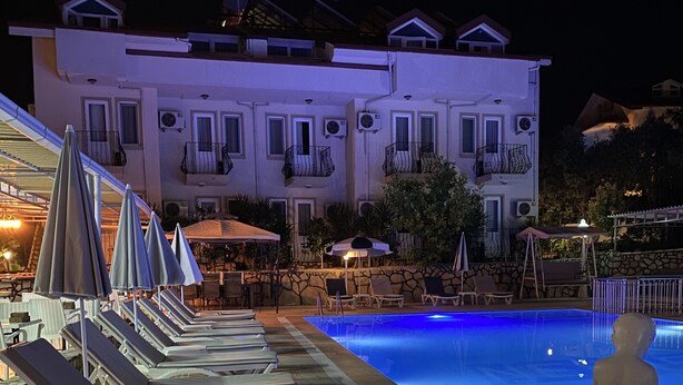 A pool area with lounge chairs and umbrellas, a stone wall, and a building with balconies in the background.