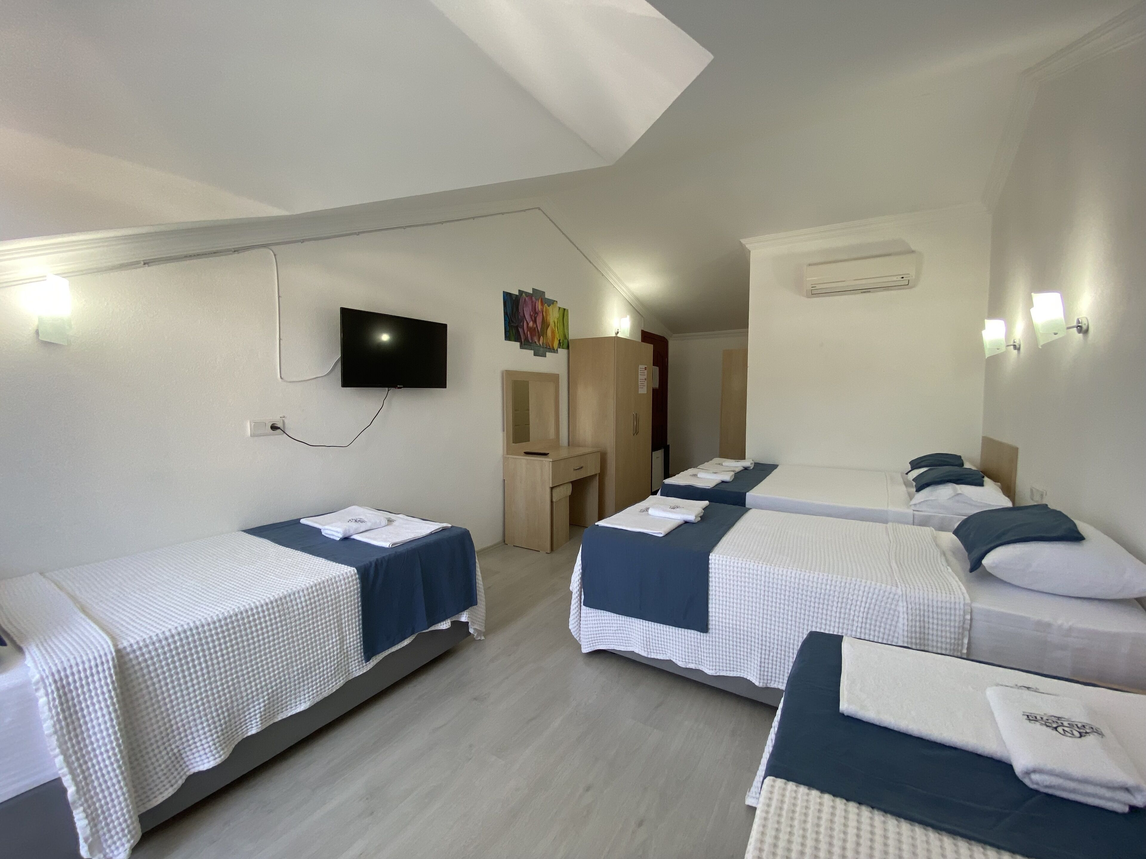 A hotel room with three single beds, a TV mounted on the wall, a desk, and a wardrobe.