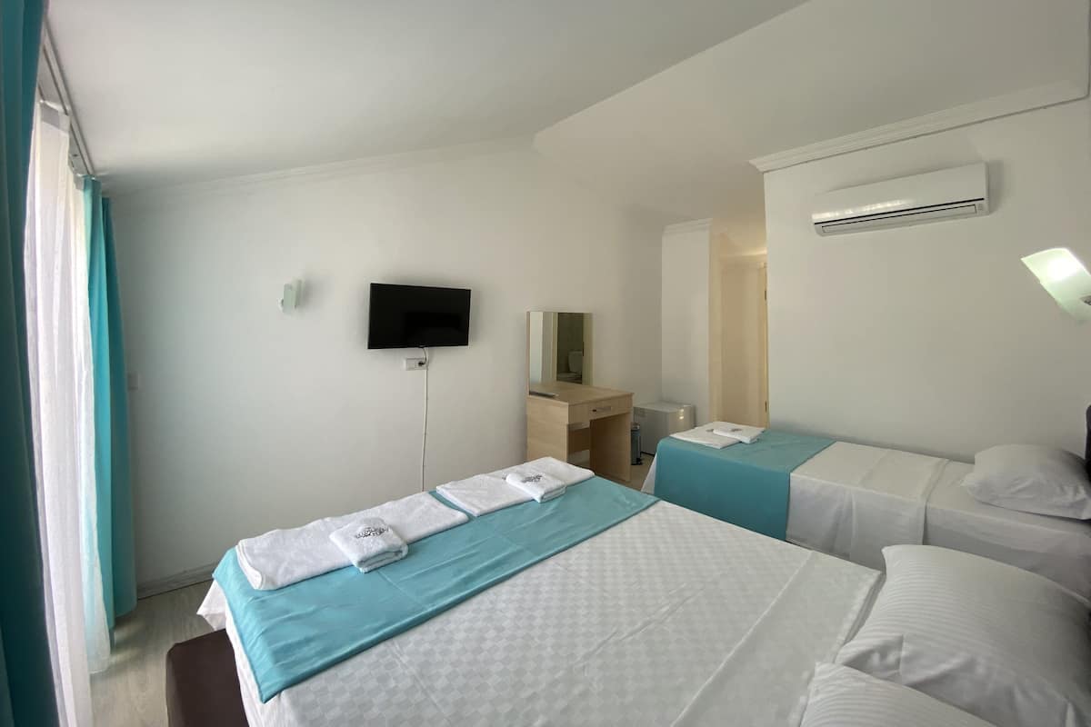 A hotel room with two beds, a TV mounted on the wall, an air conditioning unit, and a bedside table with a lamp.