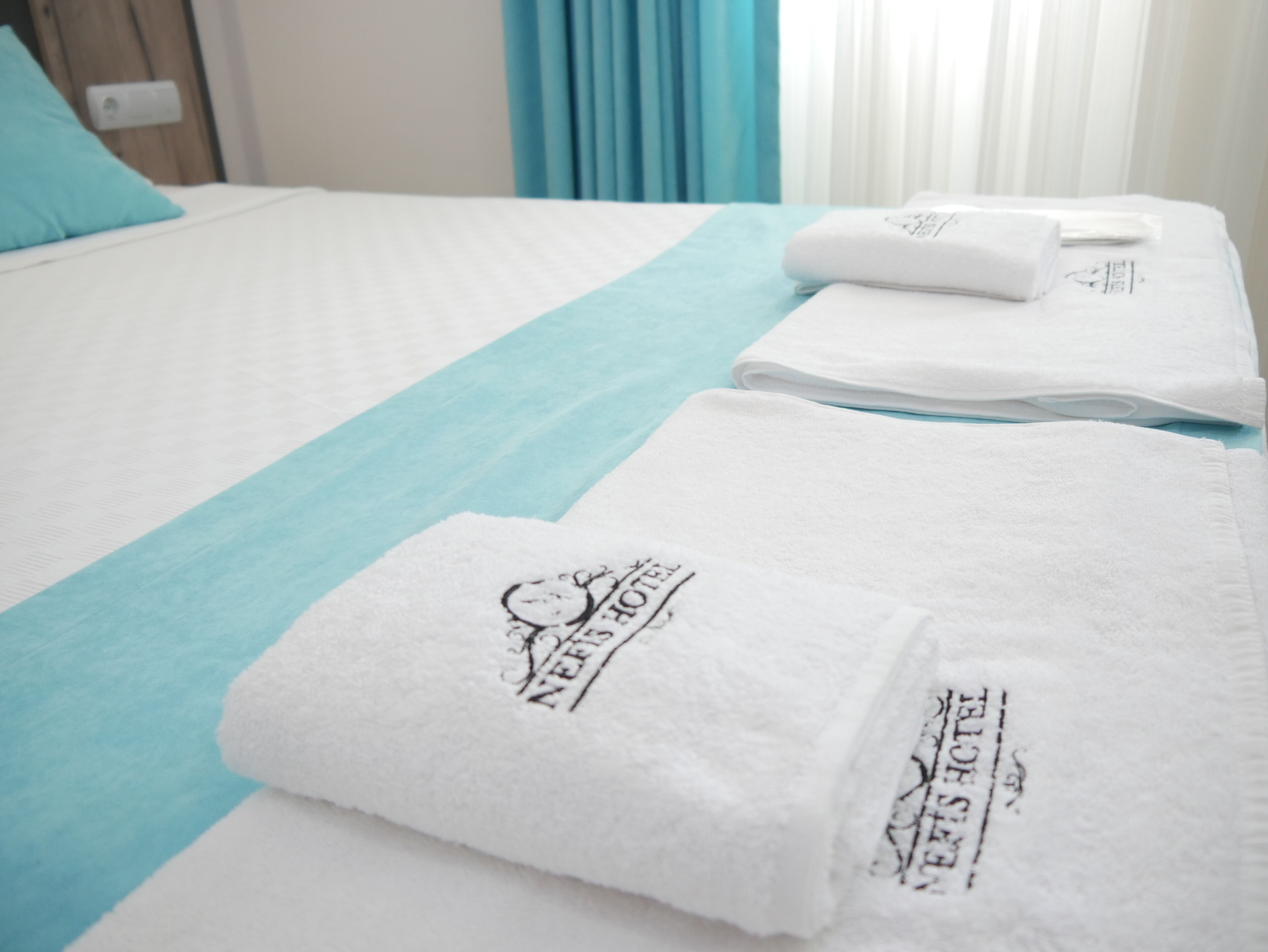 Una habitación de hotel con cama, una colcha azul y toallas blancas ordenadamente dobladas con un logotipo.
