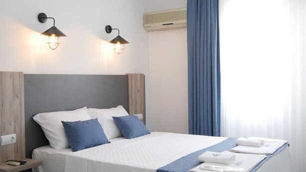 A modern hotel room with a large bed, two wall-mounted lights, an air conditioning unit, and a window with curtains. - Nefis Hotel Oludeniz (Fethiye)