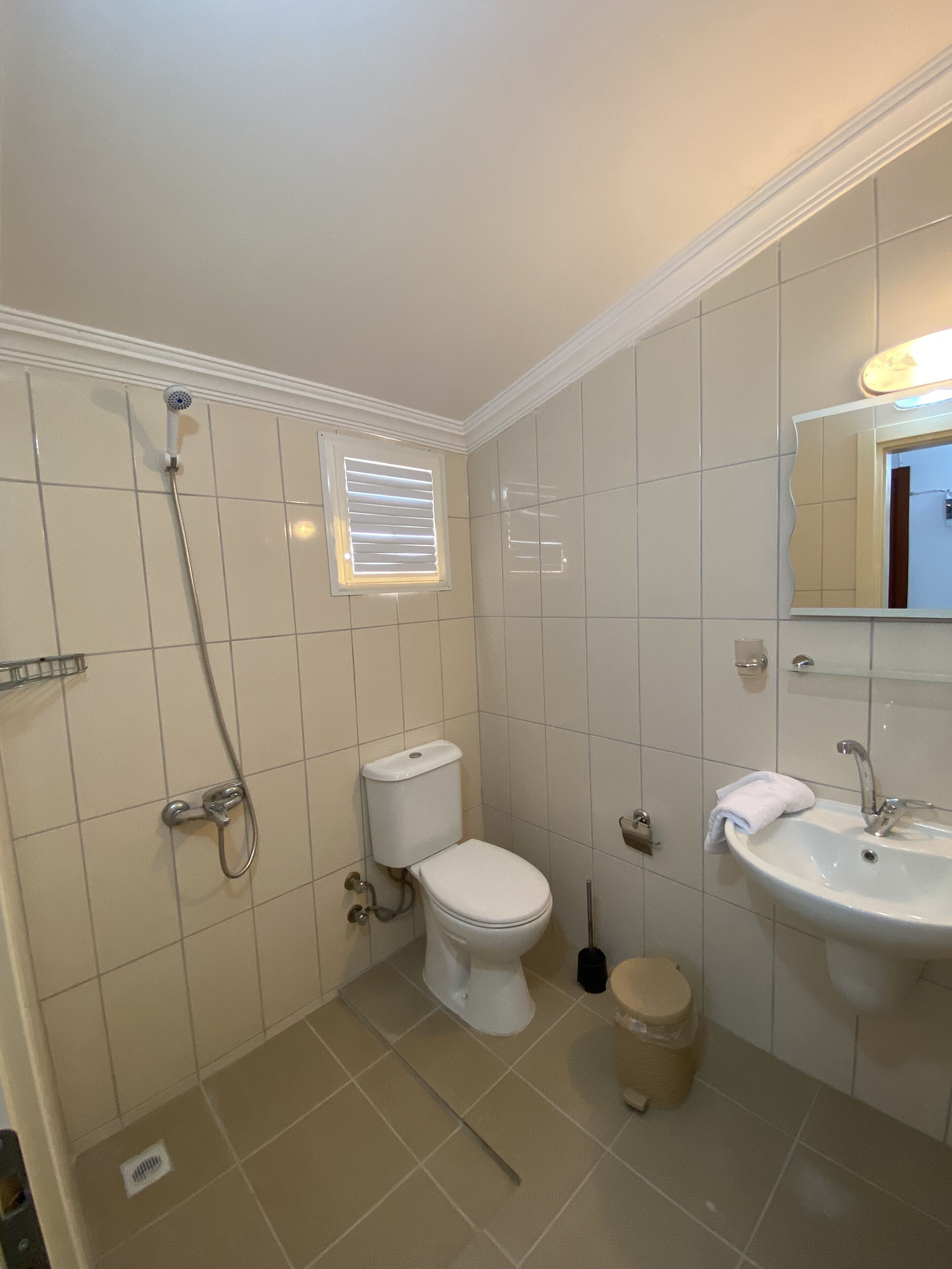 A bathroom with a toilet, shower, sink, and a window with blinds.