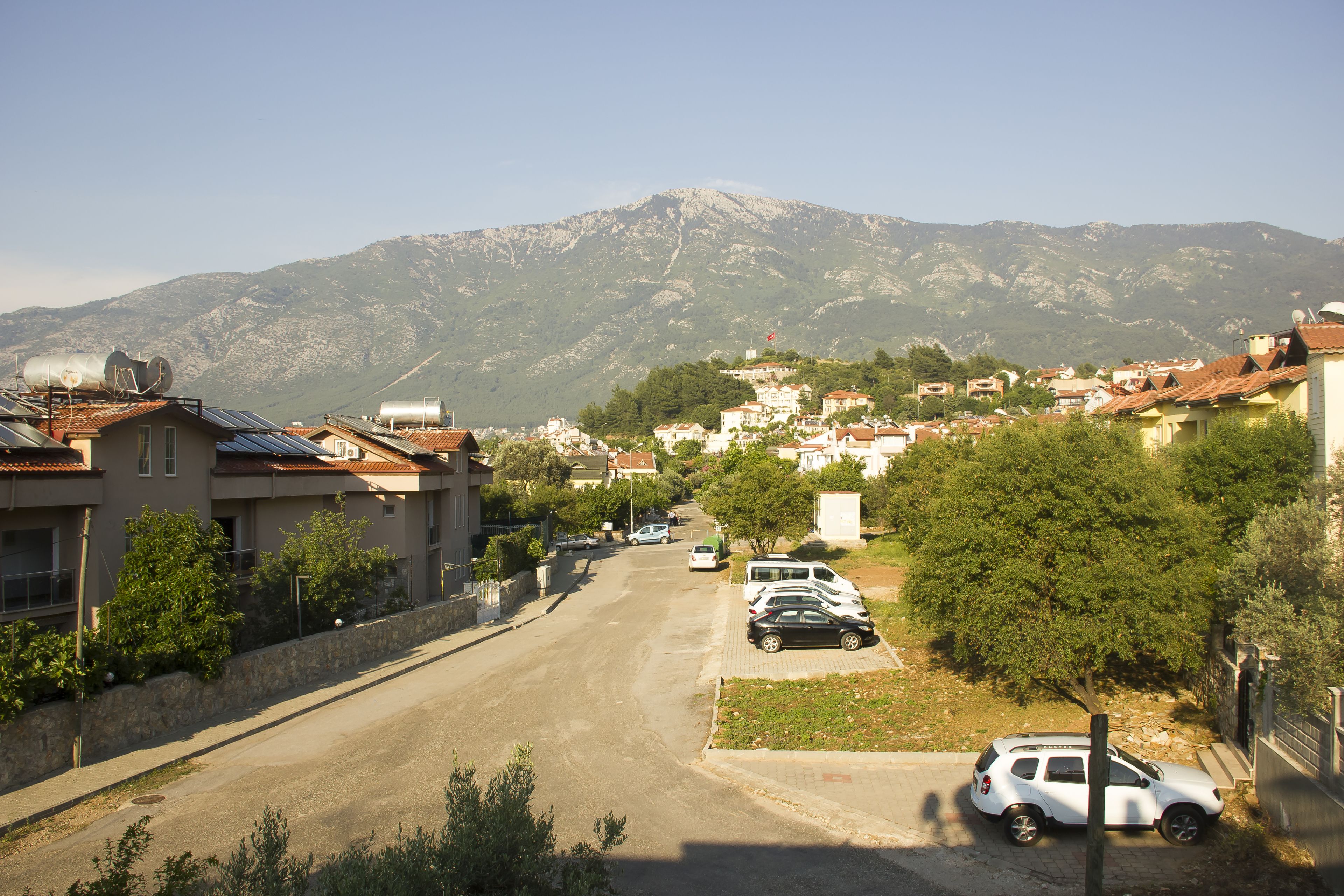 A residential street with houses, parked cars, and a mountain in the background.