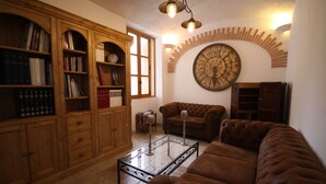 A cozy living room with a brown leather sofa, a glass coffee table, wooden bookshelves, and a large wall clock. - Aux Bords Du Temps (Zonza)
