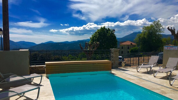 A pool area with lounge chairs, a wooden deck, and a view of mountains. - Aux Bords Du Temps (Zonza)
