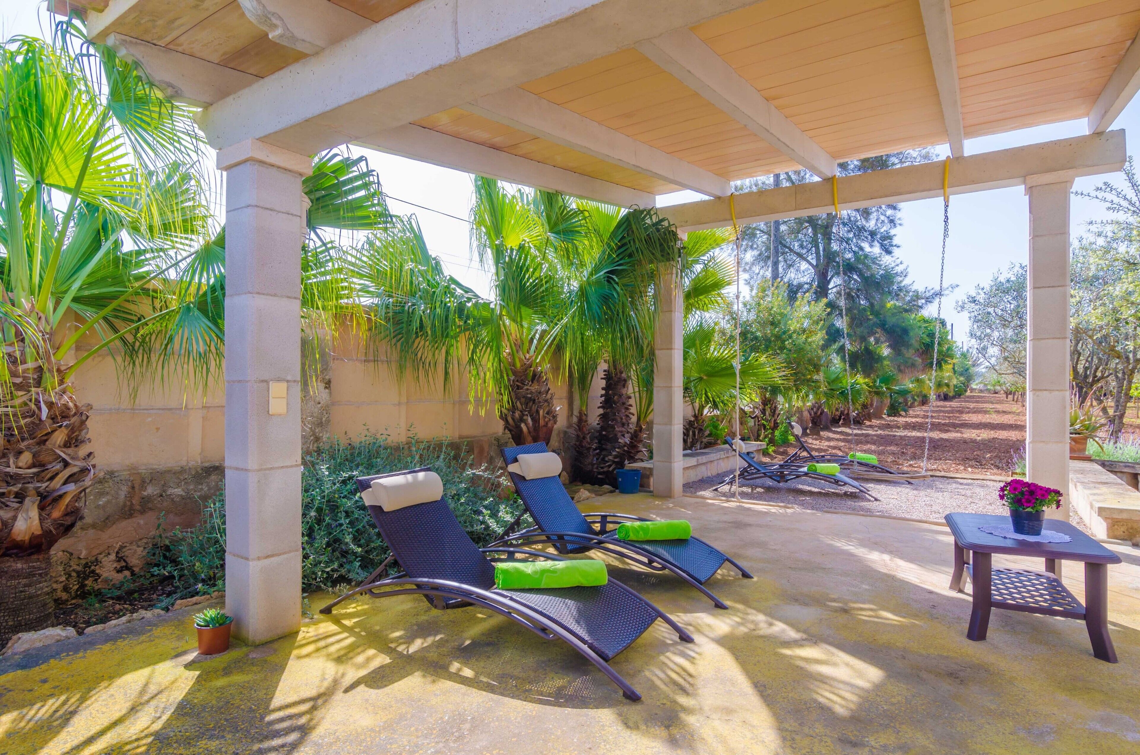 A covered outdoor seating area with lounge chairs and a small table with a flower vase.