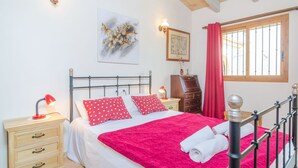 Un dormitorio con cama, mesita de noche, cómoda, ventana con cortinas y decoración en la pared.