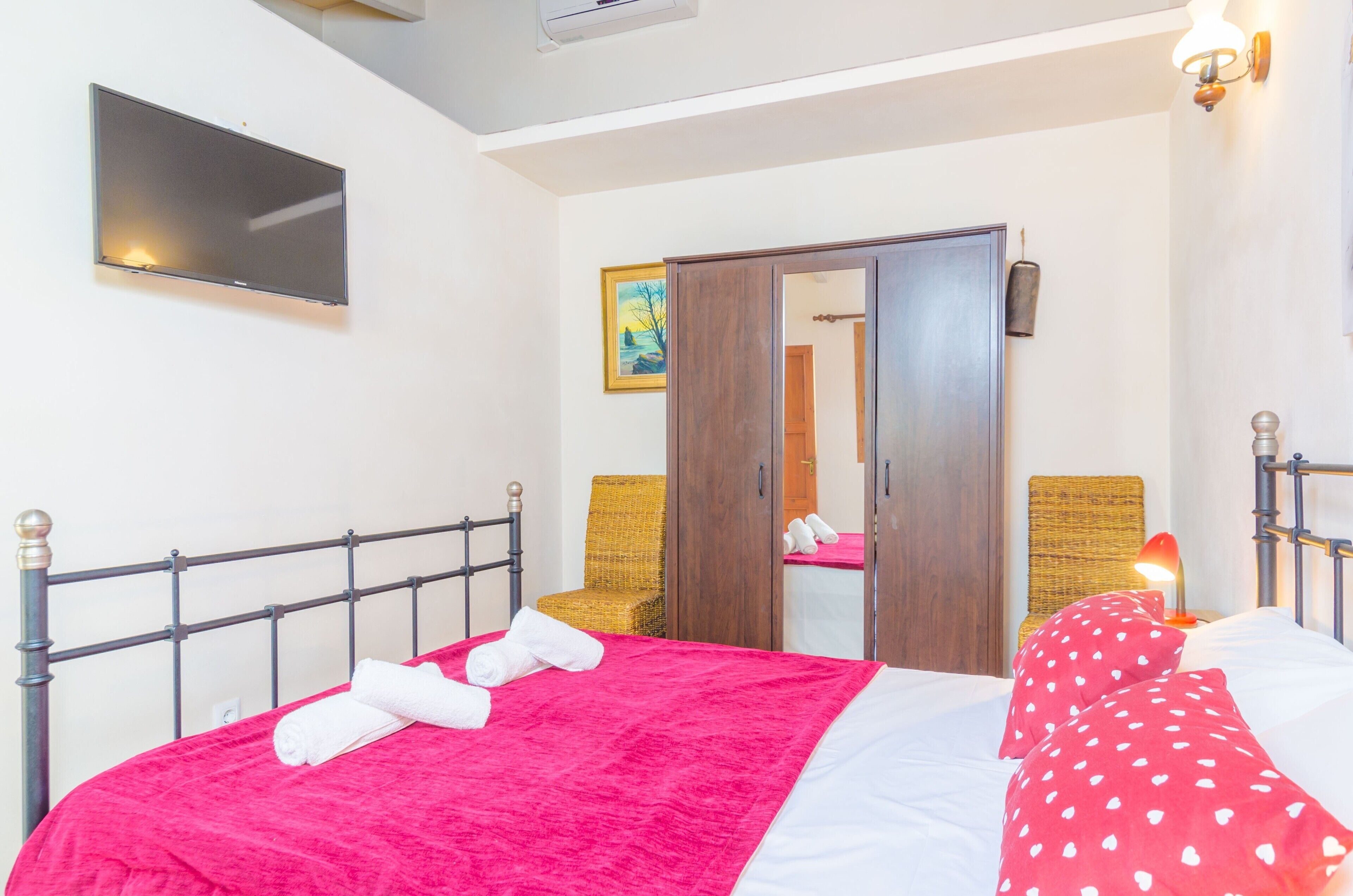 A hotel room with a bed, a flat-screen TV mounted on the wall, a wooden wardrobe, and a mirror.