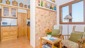 Una cocina con armarios de madera, un microondas y un comedor con mobiliario de mimbre y una mesa con revistas.