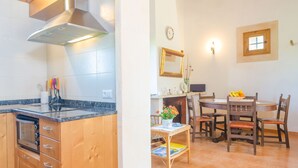 Una cocina con armarios de madera y horno empotrado, un comedor con mesa redonda y sillas, y una ventana pequeña con marco de madera.