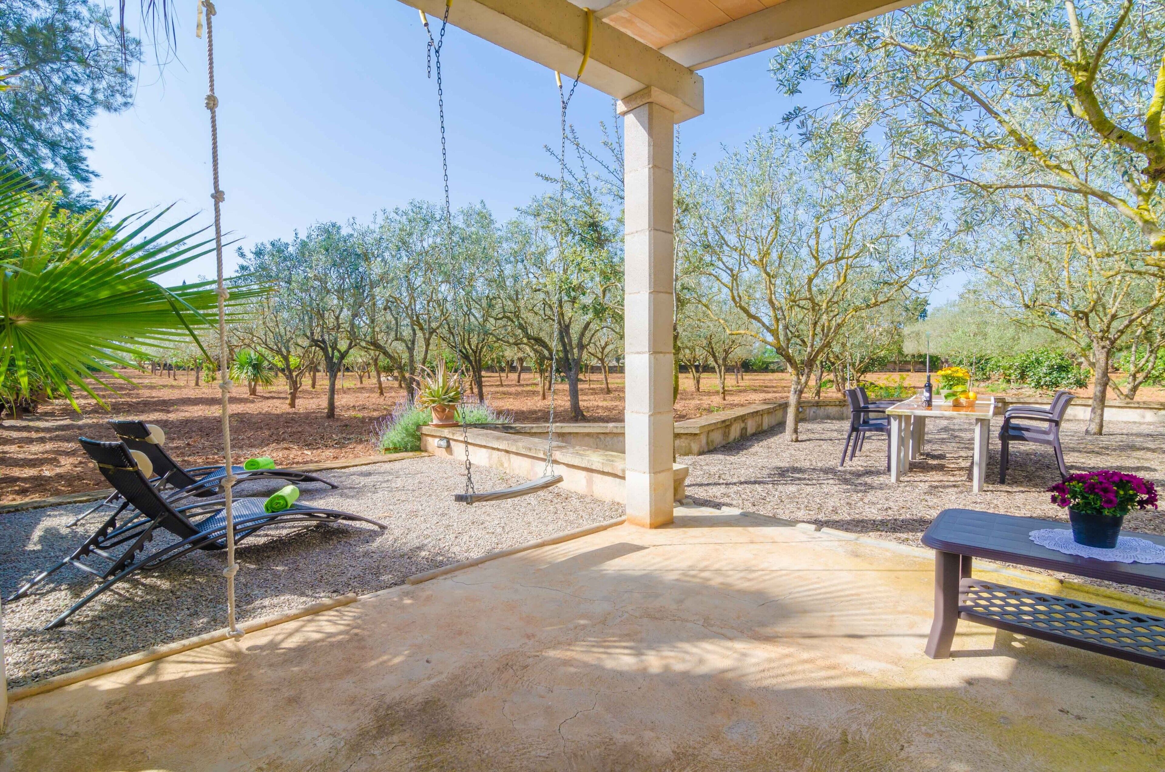Une terrasse extérieure avec une balançoire, un coin salon et une table avec des chaises.