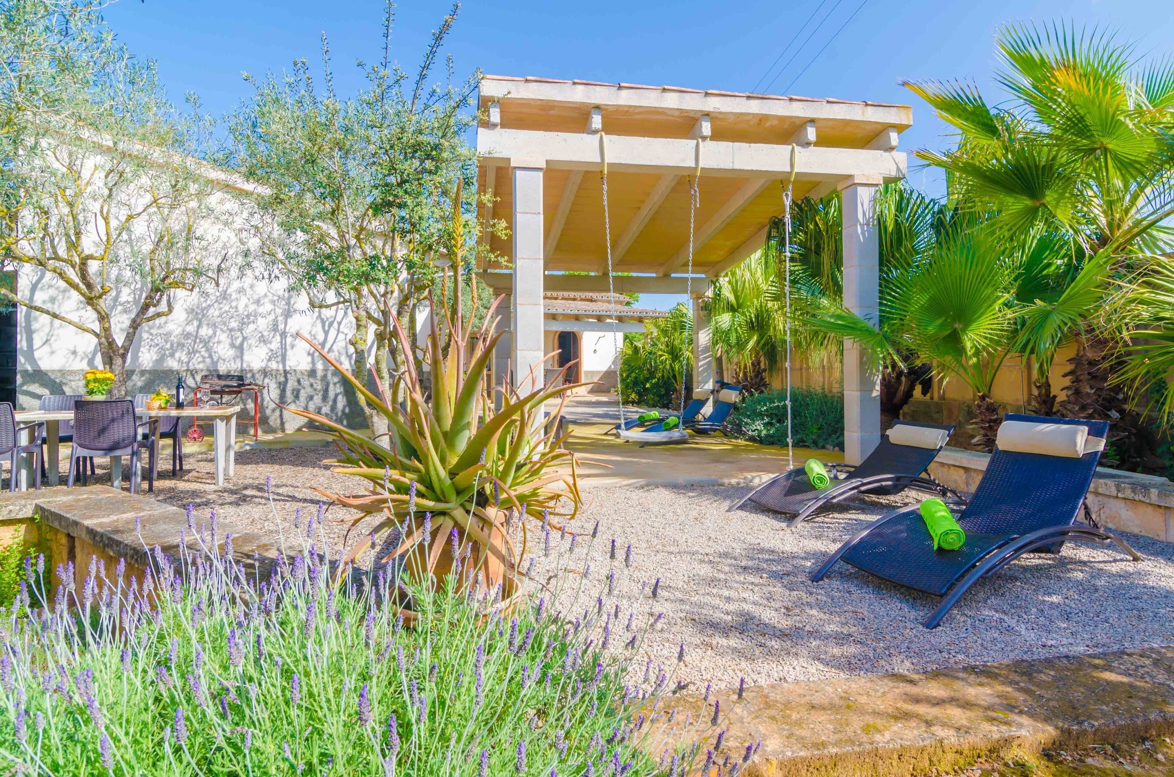 Un espacio de estar al aire libre cubierto con mesas y sillas, rodeado de plantas y una pequeña piscina.