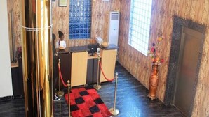 Een receptiezone met een houten inrichting, een receptiebalie, een incheckbalie en een rode loper naar de ingang.