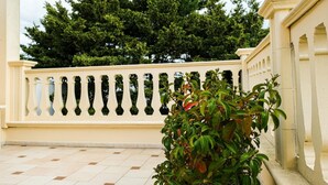 A balcony with a beige railing, a tiled floor, and a large tree in the background. - Olimpo B&B (Giurdignano)
