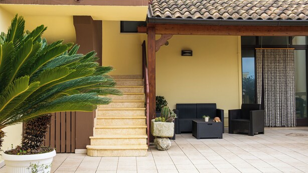 A covered outdoor area with a staircase, outdoor seating, and a large potted plant. - Olimpo B&B (Giurdignano)