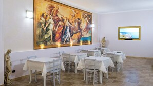 A dining area with tables and chairs, a large mural on the wall, and a television screen. - Olimpo B&B (Giurdignano)