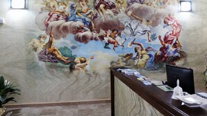 A mural with classical figures and a reception desk with a computer and papers. - Olimpo B&B (Giurdignano)