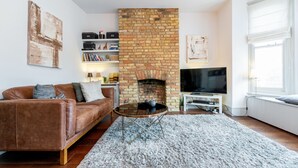 A living room with a brick fireplace, leather sofa, and a flat-screen TV. - Vauxhall Park Views - 2 Bed Flat by BaseToGo (London)