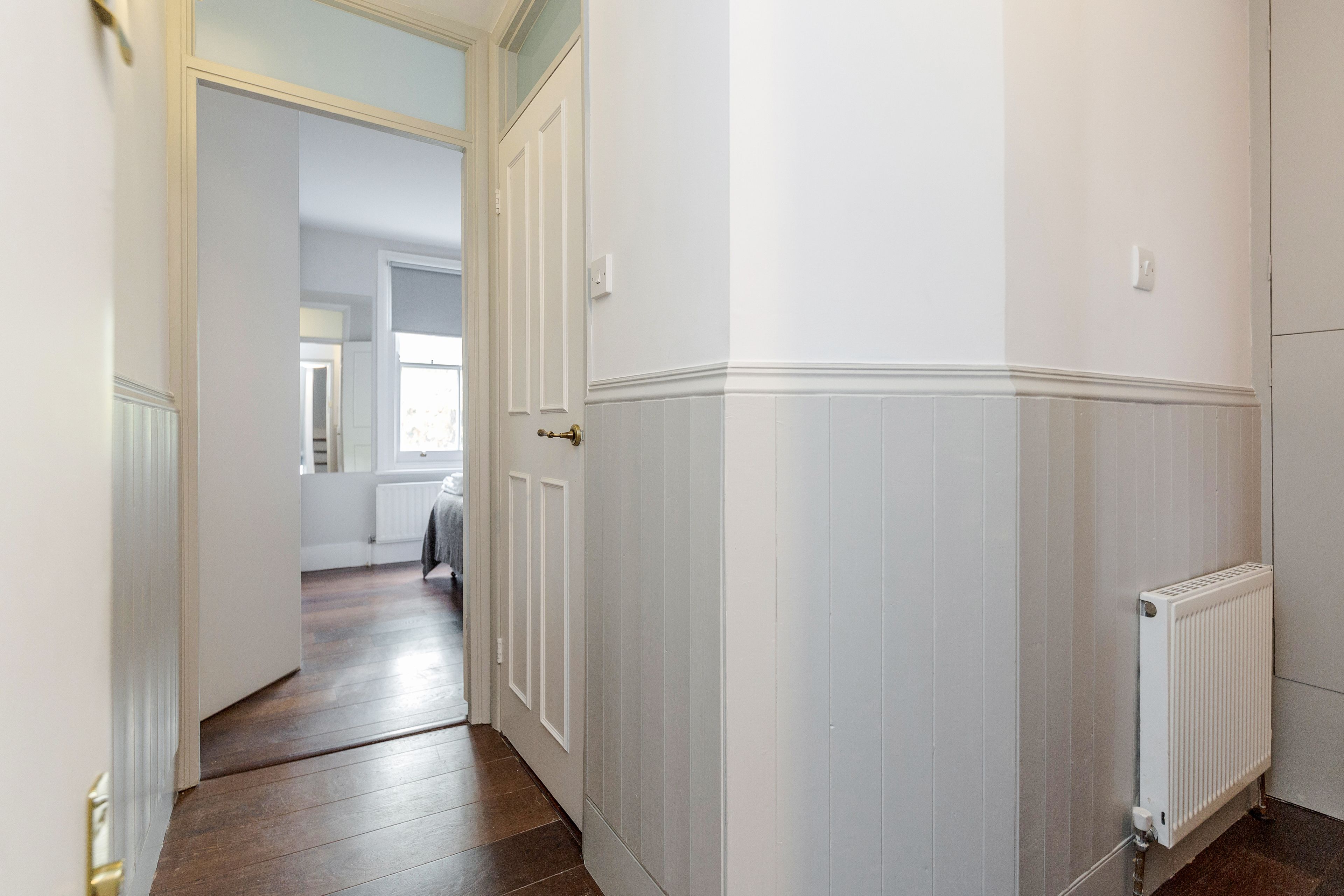 A hallway with white wainscoting and a radiator.
