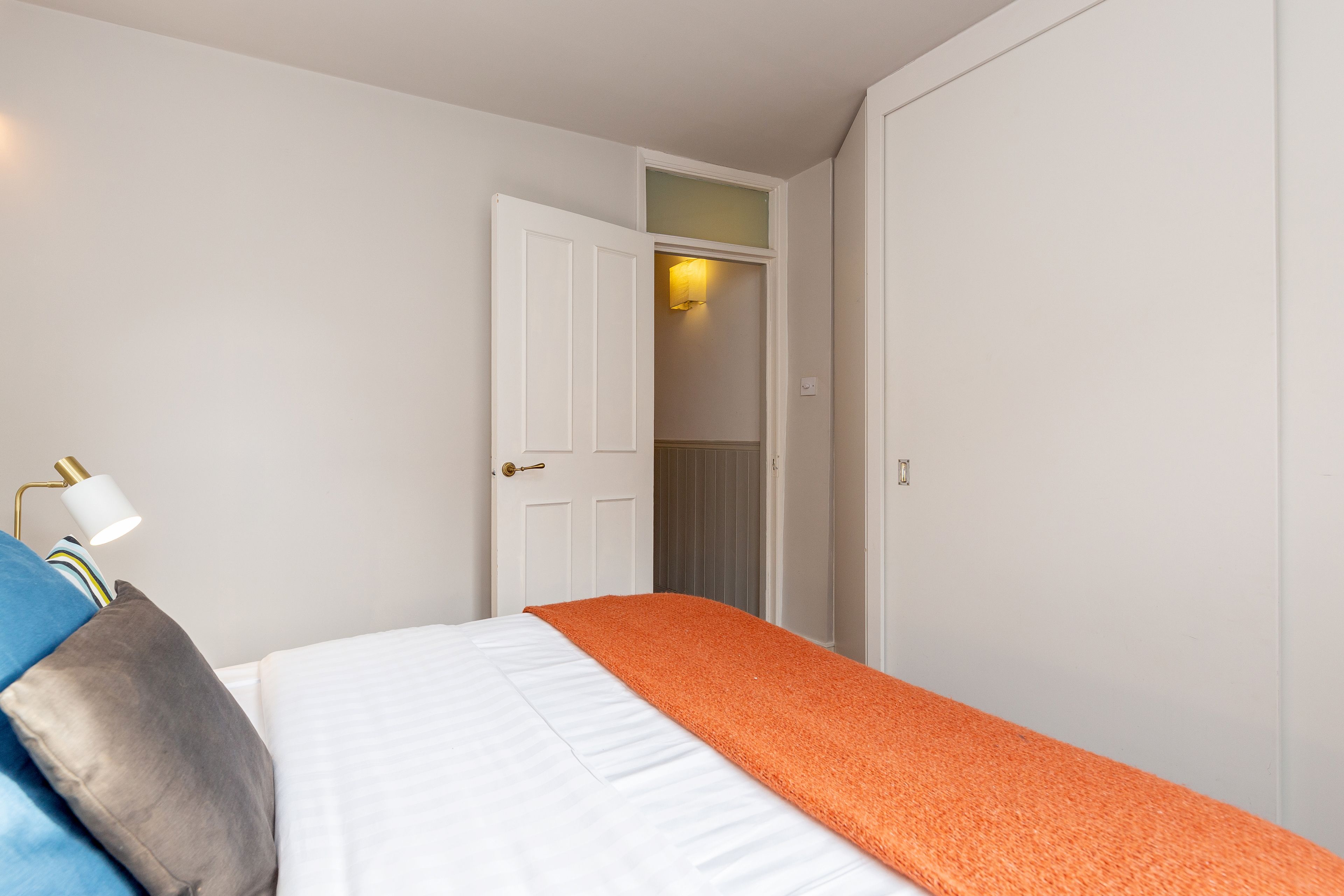 Un dormitorio con cama, una mesita de noche, una lámpara y una puerta que da al baño.