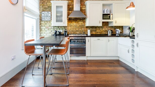 A modern kitchen with white cabinets, a brick wall, a stainless steel range hood, and a dining area with a table and chairs. - Vauxhall Park Views - 2 Bed Flat by BaseToGo (London)