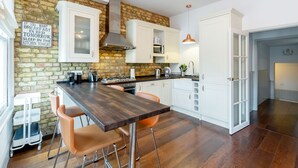 A modern kitchen with a brick wall, white cabinetry, and a wooden bar counter. - Vauxhall Park Views - 2 Bed Flat by BaseToGo (London)