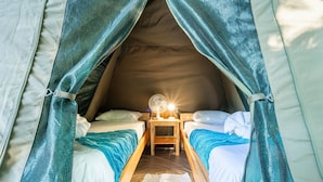 Ein Zelt mit zwei Betten, einem Nachttisch mit Lampe und einem Ventilator.