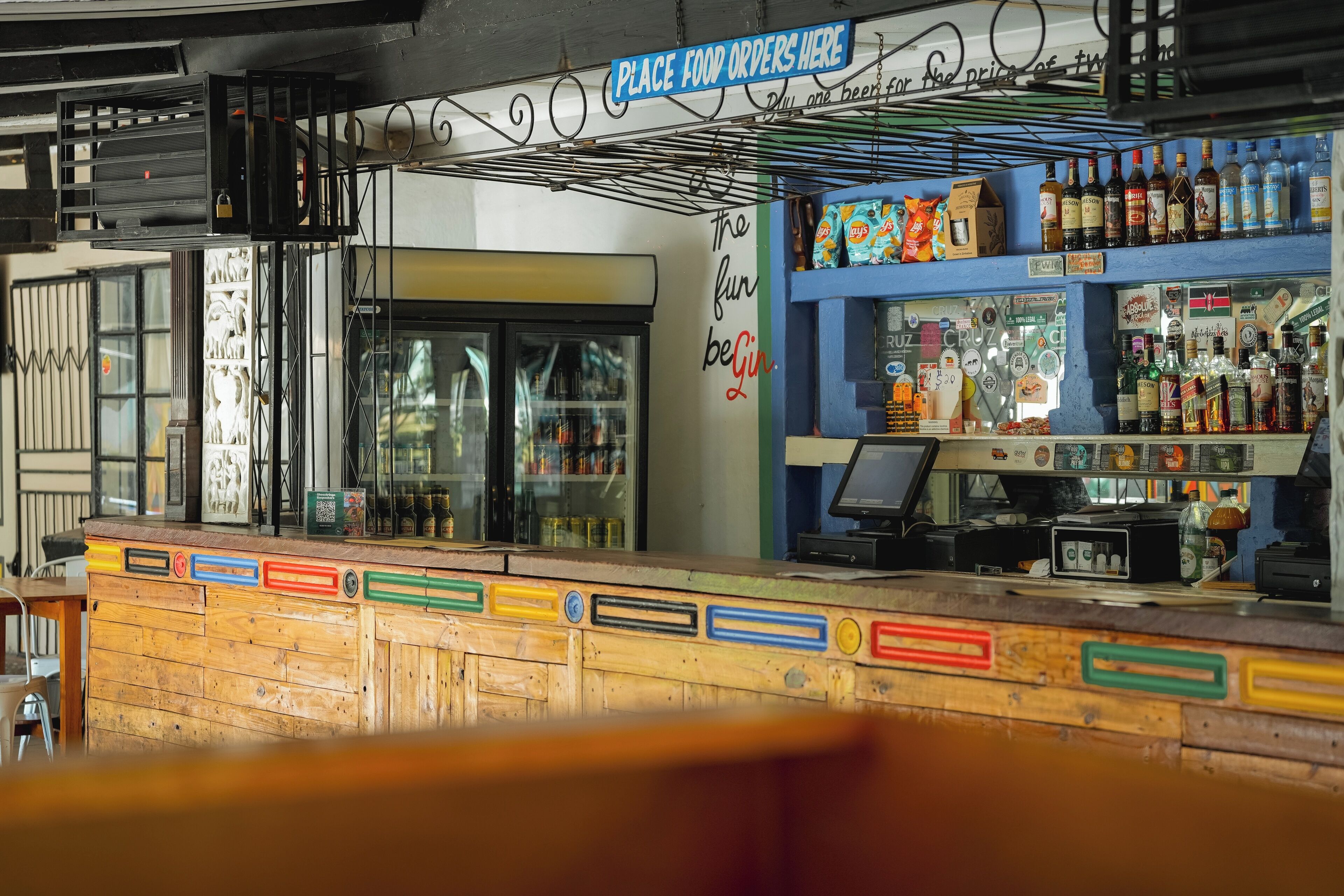 Una zona de bar con mostrador de madera, una caja registradora y estantes llenos de botellas y aperitivos.