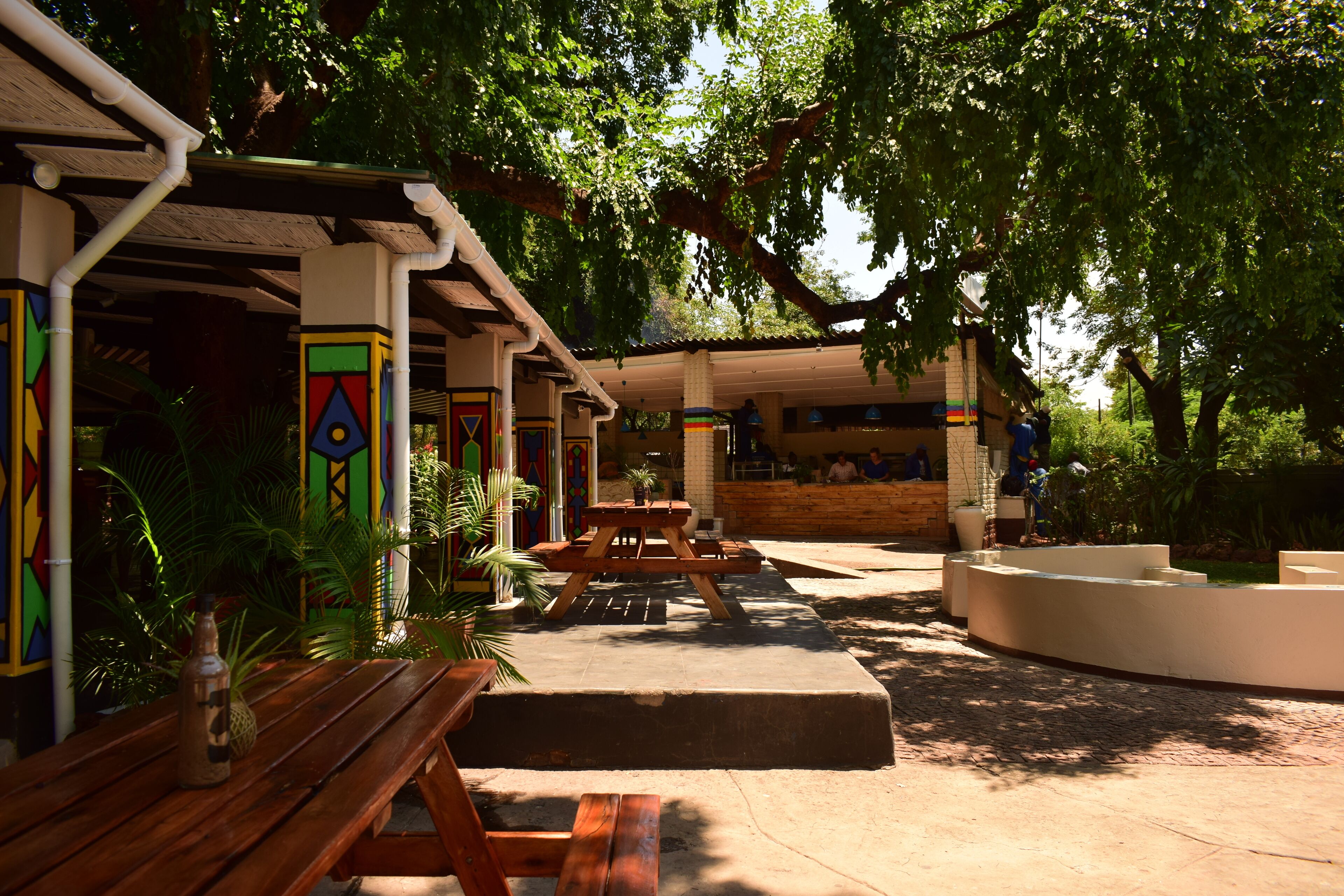 An outdoor patio area with wooden benches and tables, surrounded by lush greenery and trees.