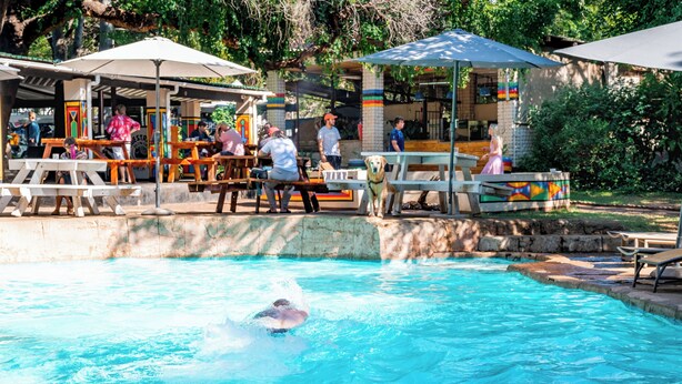 Ein Schwimmbecken mit Personen, Bänken und Sonnenschirmen.