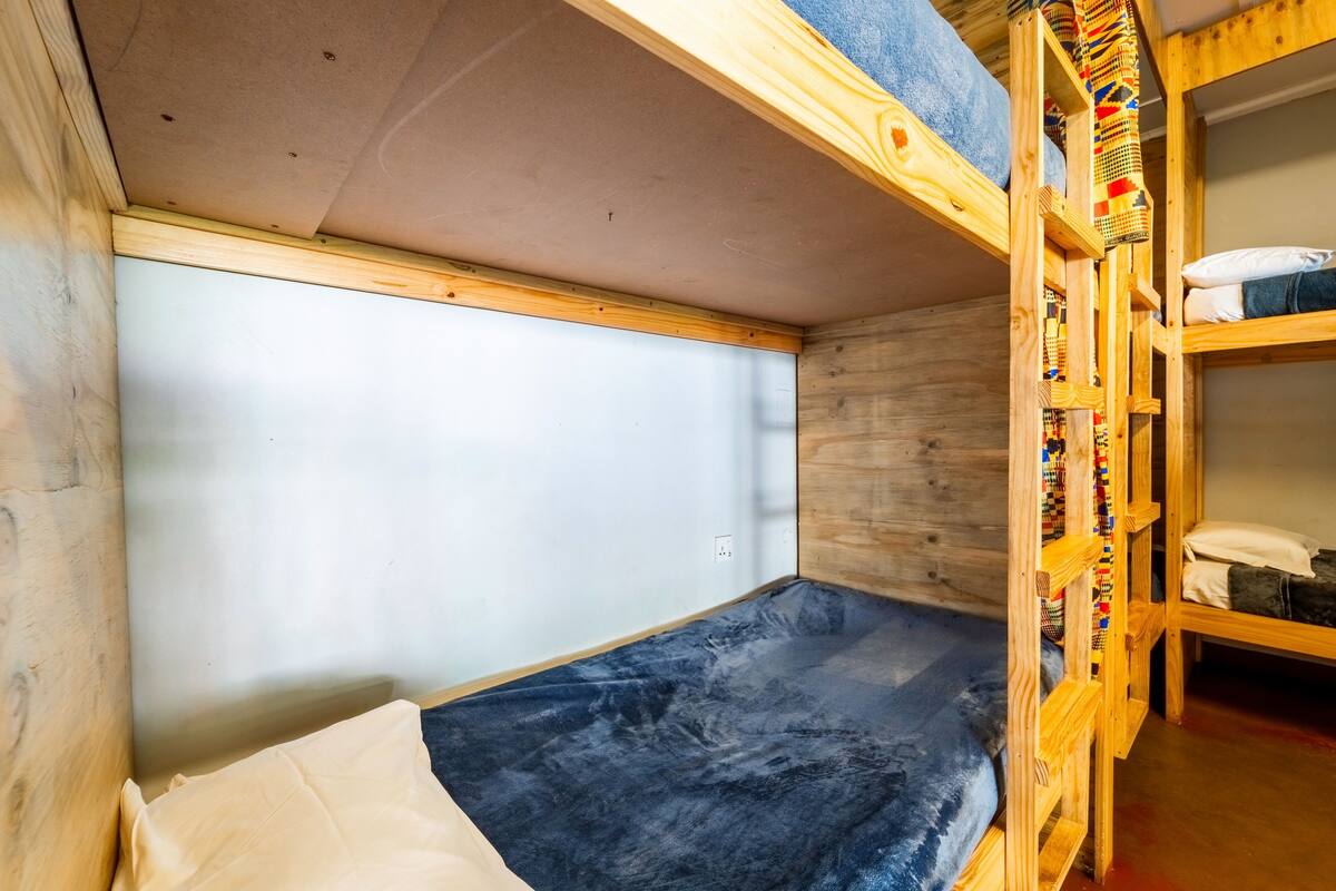 A compact room with a bunk bed, a small window, and a wooden wall.