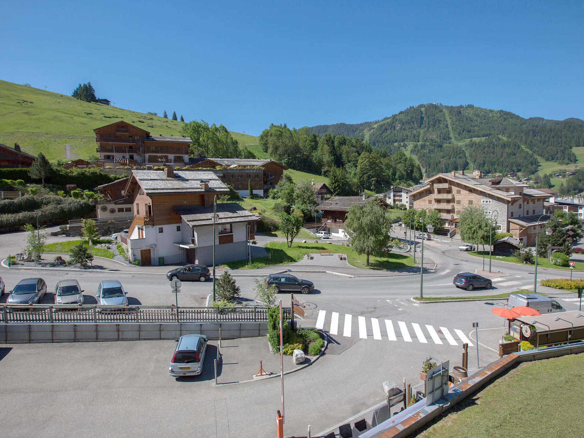 Un hotel con estacionamiento, un paso de peatones y vistas a una colina verde.