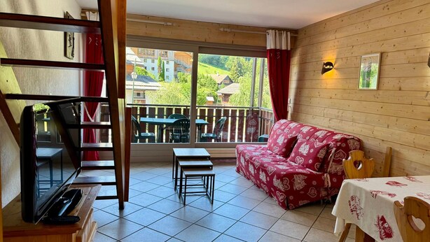 A room with a balcony, a sofa, a table, and a TV. - 2-Bedroom Duplex near Ski Slopes, Central Village, Parking, Balcony, La Clusaz (La Clusaz)