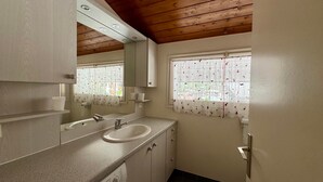 A bathroom with a sink, mirror, window with patterned curtains, wooden ceiling, and a tiled floor. - 2-Bedroom Duplex near Ski Slopes, Central Village, Parking, Balcony, La Clusaz (La Clusaz)