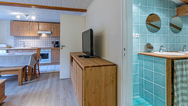 Una cocina compacta con armarios de madera, una mesa de comedor y un televisor sobre un mueble de madera.