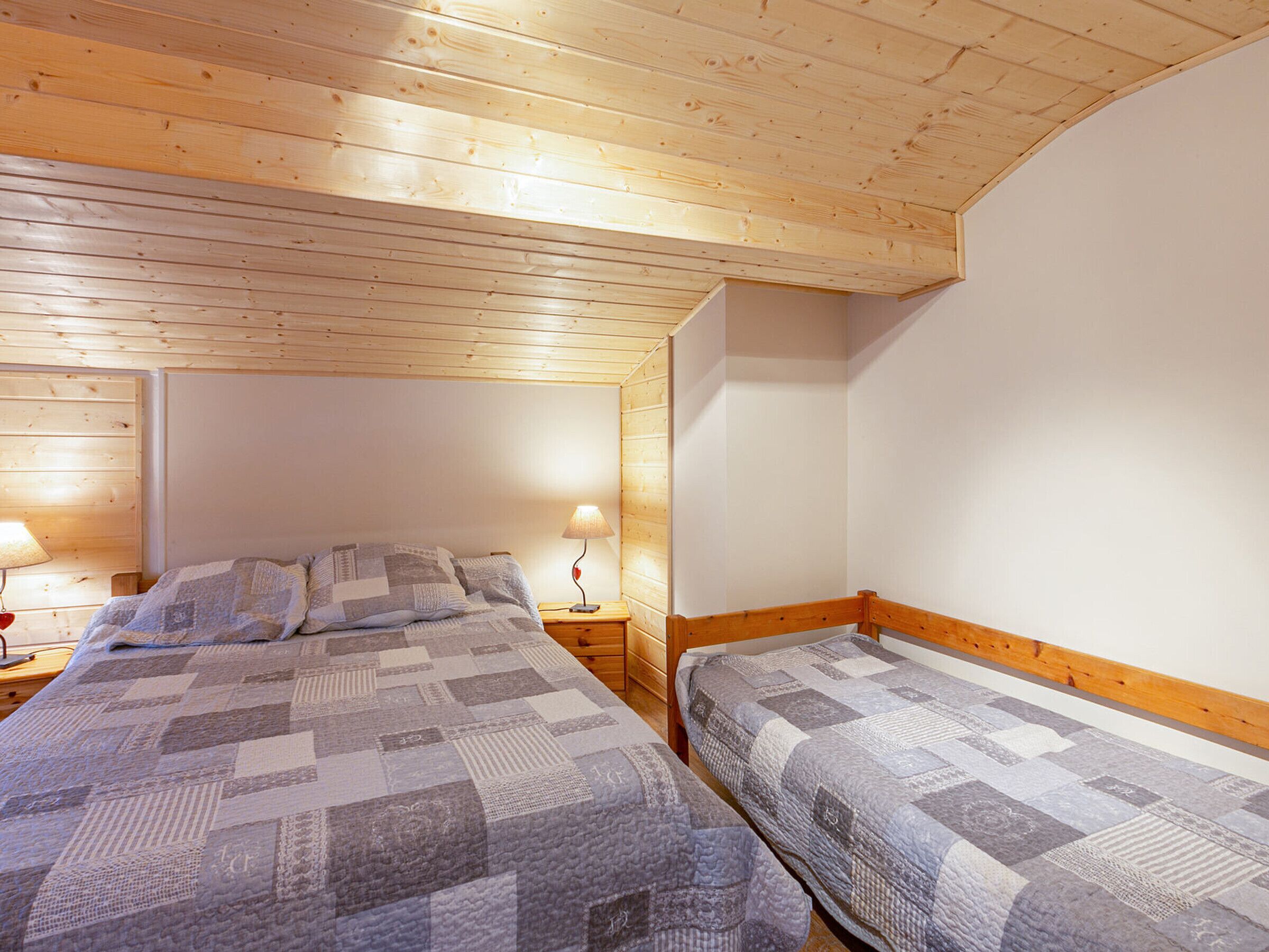 A bedroom with two single beds, wooden ceiling, and bedside lamps.