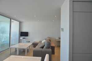 A modern living room with a sofa, a TV, and a glass wall.