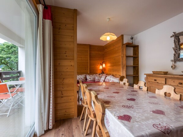 Een knus houten vertrek met een bed, een tafel, stoelen en een hanglamp.