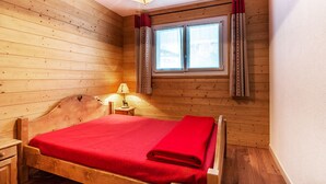 A wooden room with a bed, a nightstand, a lamp, and a window with curtains.