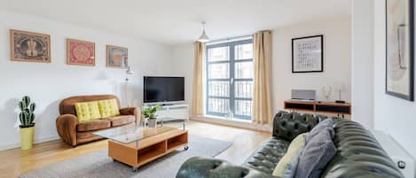 A modern living room with a brown sofa, a green sofa, a glass coffee table, and a flat-screen TV.