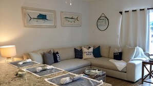 Een woonkamer met een beige bank, een granieten aanrecht met handdoeken, en twee ingelijste schilderijen van vissen aan de muur.