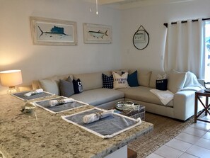 A living room with a beige sofa, a granite countertop with towels, and two framed fish paintings on the wall.