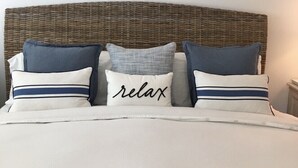 Een bed met een geweven hoofdbord, drie kussens en twee ingelijste visdecoraties aan de muur.