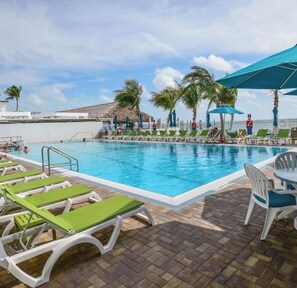A swimming pool with lounge chairs and umbrellas, surrounded by palm trees and a clear sky.