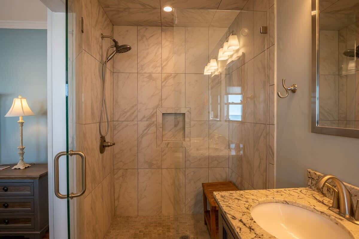 A modern bathroom with a glass-enclosed shower, a marble sink, and a vanity with a mirror.