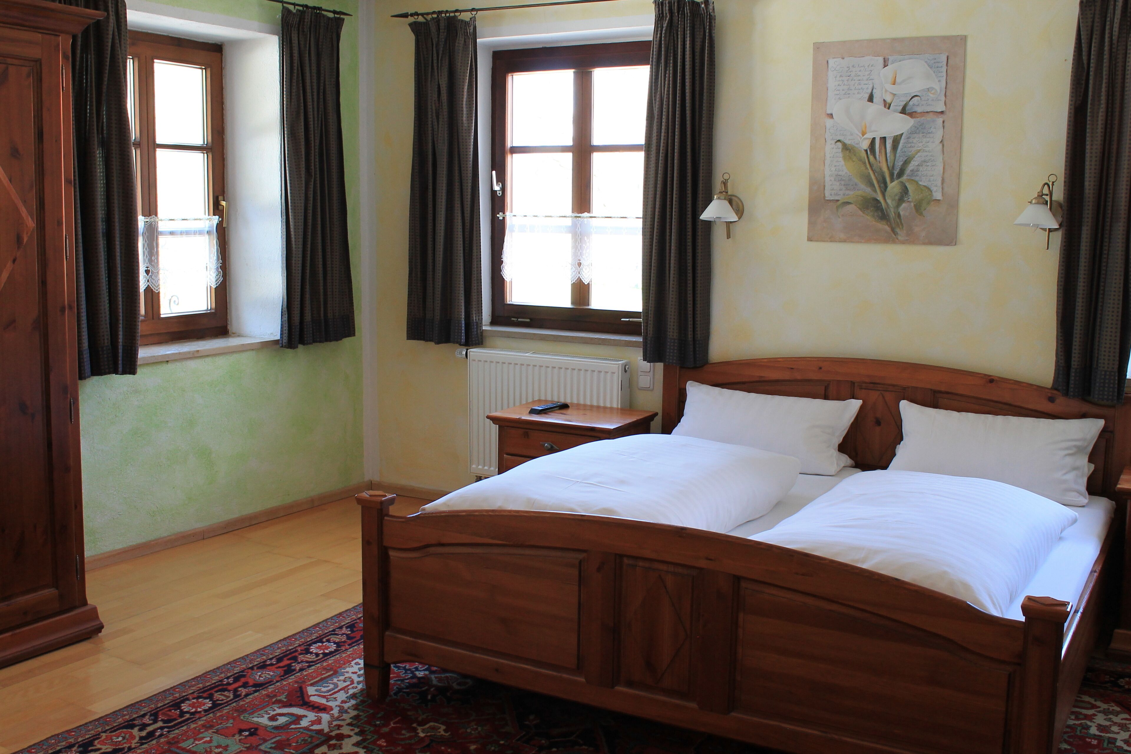 Een houten bed in een kamer met een raam, een radiator en een wandlamp.