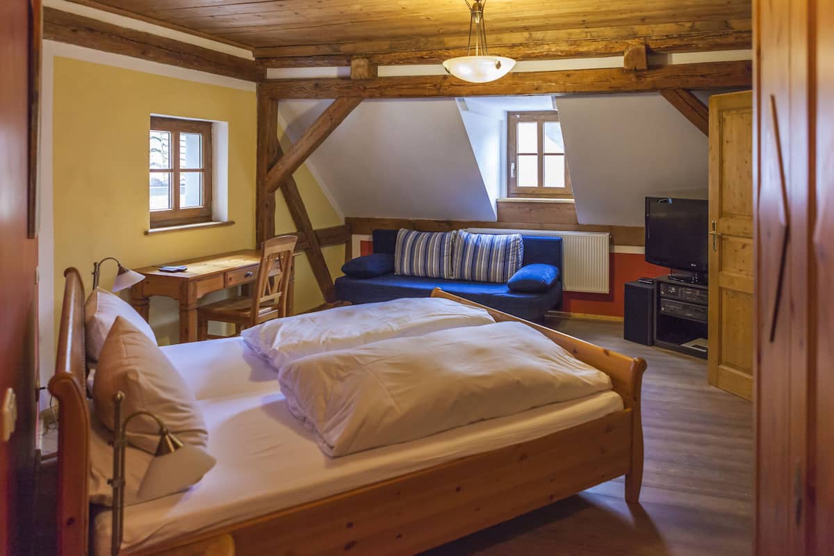 Een knus zolderkamertje met een houten bed, een blauwe bank en een televisie.